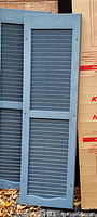 One shutter leaning against wall showing blue-grey color and louver design