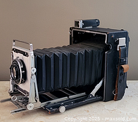 Front three-quarter view of Crown Graphic camera, bellows extended, showing lens, shutter, and bed.