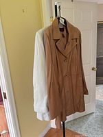 Camel brown leather coat and light grey jacket hanging on stand
