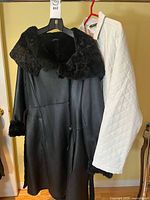 Front view of black Danier shearling coat beside white quilted jacket