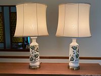 Front view of both ceramic lamps lit, showing leaf design, shades, bases