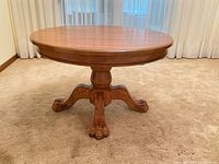 Full view of round wood pedestal table showing base and lion’s paw feet