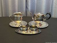 Group shot showing teapot, pedestal creamer on their respective round trays, and cream & sugar set on oval tray