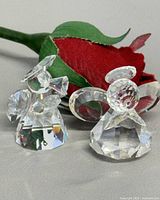 Both Swarovski crystal angel figurines beside fabric rose