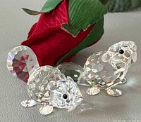 Both Swarovski crystal beaver figurines beside red fabric rose