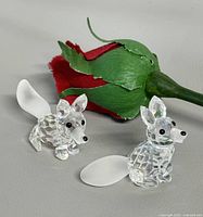 Both Swarovski crystal fox figurines beside artificial rose
