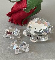 Group view of three crystal turtle figurines with red fabric rose for scale