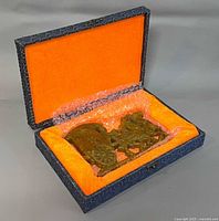 Carved stone ornament inside open brocade box with orange lining