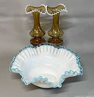 White milk glass bowl with blue ruffled edge front view, two amber ruffled vases behind