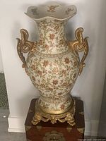 Full view of porcelain vase on pedestal showing floral design and gilded handles