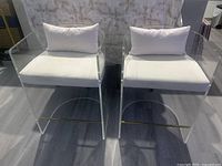 front view of both clear acrylic stools with white seat cushions and pillows