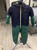 Front view of Patagonia navy/green one-piece snowsuit hanging