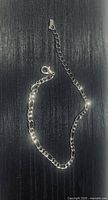 Sterling silver chain anklet coiled on black background