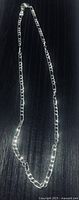 Full view of entire sterling silver Figaro chain necklace on dark surface