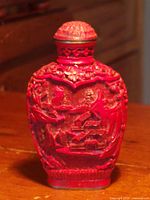 Front view of red cinnabar snuff bottle with carved landscape scene