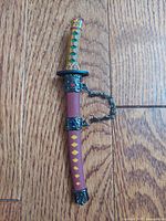 Full view of miniature sword in scabbard on wood background