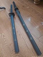 Two black scabbarded swords on hardwood floor showing overall lengths and kanji