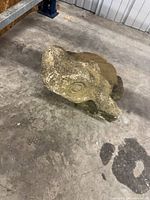 Side view of weathered cast concrete frog statue lying on its side showing texture and patina