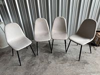 Front view of all four beige padded chairs with black legs