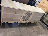 Front view of ivory French Provincial dresser showing all six drawers, center lattice door, cabriole legs