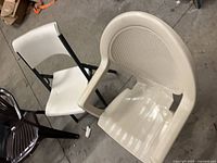Top view of beige resin armchair and white folding chair alongside part of brown armchair
