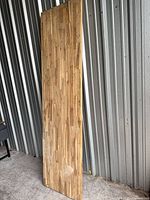 Full view of the tall rectangular wood slab leaning against corrugated wall