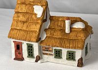 Front view of porcelain cottage showing sign, door, windows, thatched roof with snow