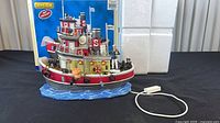 Full view of Lemax Salty the Tugboat model showing corded switch and box backdrop