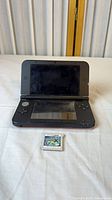 Nintendo 3DS XL open with screen visible and Pokémon X cartridge in front