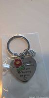 Close-up of a single keychain showing heart charm with engraved message, enamel flower, small heart charm