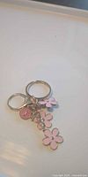 Close-up of one keychain showing pink enamel flower charms and round disc charm on metal split ring