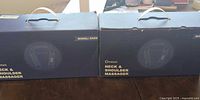 Two boxed KNQZE neck & shoulder massagers on table
