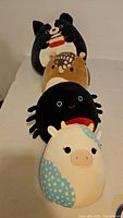 Four Squishmallows lined up: cat, hedgehog, spider, cow