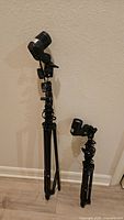 Two black metal light tripods of different heights standing against wall
