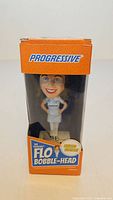 Front view of sealed box showing Progressive branding and Flo bobble-head inside