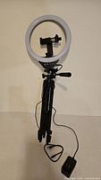 Ring light mounted on tripod with cable and adapter visible