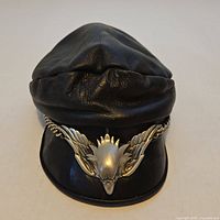 Front view of black leather biker cap showing eagle emblem and chain trim