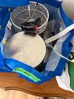 Blue bag labeled Bathroom containing metal waste bin, wire mesh basket and boxed razors