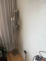 Full view of silver floor lamp in corner showing three chain-fringe light heads and base