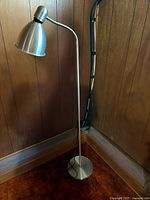 Full view of brushed metal floor lamp showing shade, adjustable neck, pole, base, and cord