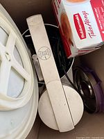 Top view of box showing Rubbermaid TakeAlongs pack, white potato ricer, metal lid, plastic lids