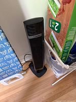 Front view of black Lasko tower heater standing on wood floor with cord visible