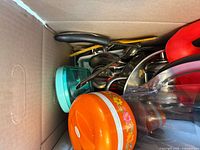 Top view of box showing orange floral container, stainless saucepan, utensils, turquoise container