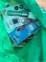 Green bag opened showing notebook, flashlight package, index cards pack, staples box and other stationery