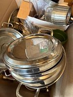 Stack of stainless steel lids, cheese grater, prep bowl, utensils visible in box