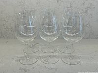 Six clear Riedel wine glasses side by side on counter