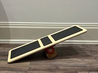 Side view of balance board showing deck, grip pads, red pivot, wooden rocker