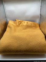 Folded golden yellow wool blanket with satin binding shown in neutral light