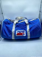 front view of blue duffel showing Pepsi logo and white handles