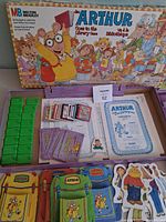 Open box with lid, green plastic book tiles, card deck, backpack and character pieces visible